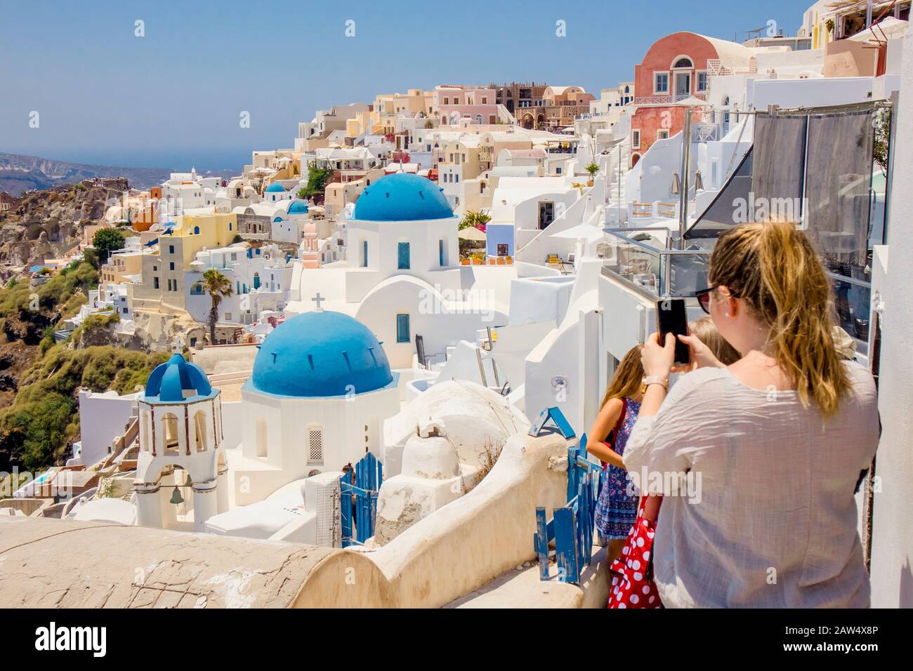 Famous blue dome orthodox church in village of Oia on Santorini island in Greece in Europe. Young female woman tourist taking a picture with smartphon Stock Photo