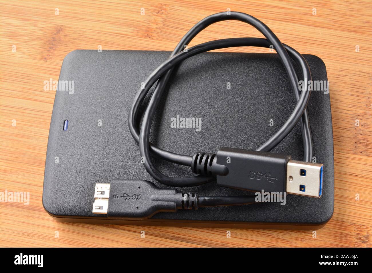 Black and flat external USB 3.0 hard disc with coiled USB 3.0 cable on wooden background, view from above Stock Photo