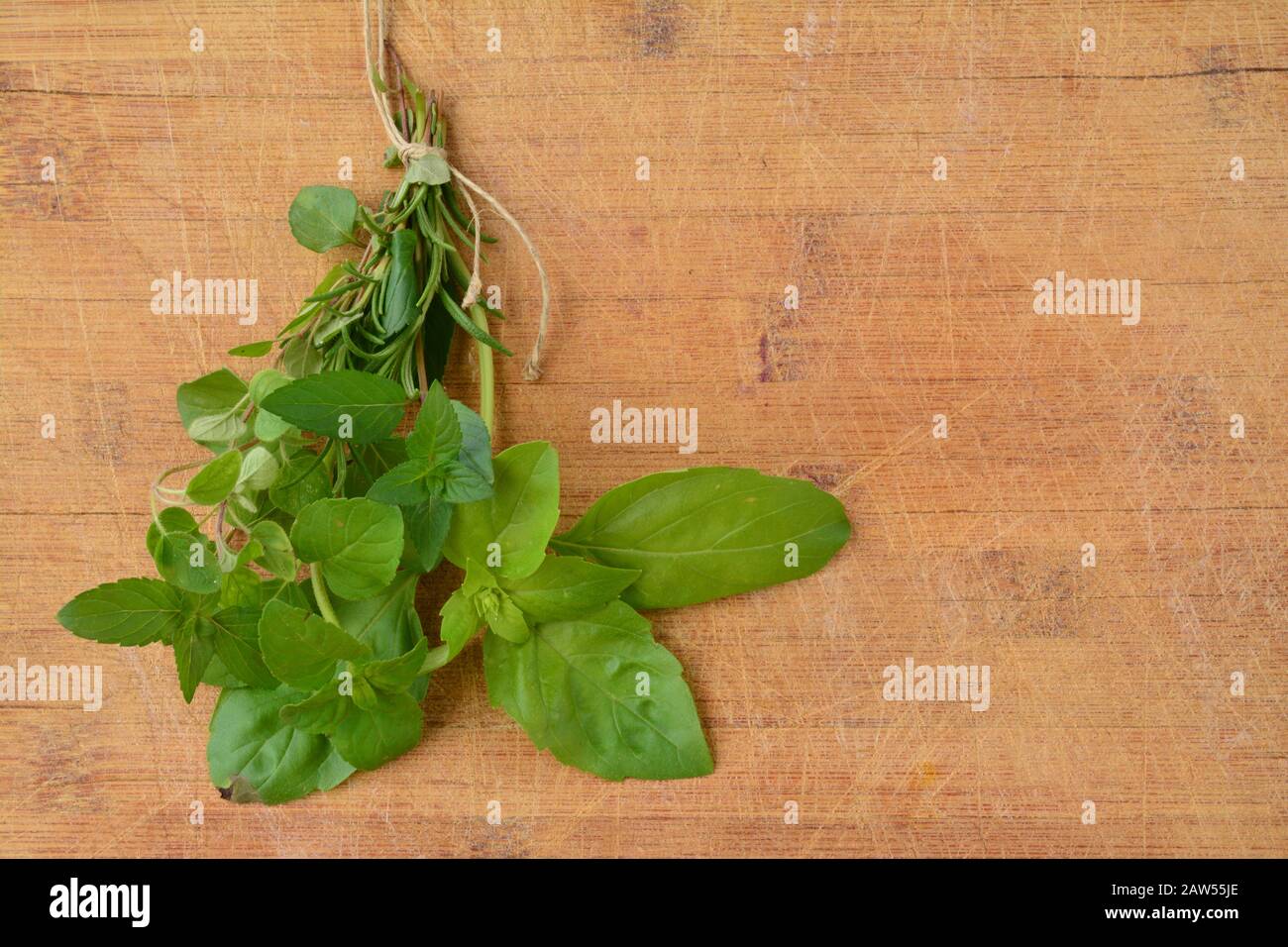Fresh green aromatic plants, basil, rosemary, peppermint,  mojito mint and oregano tied in a bunch over wooden background Stock Photo