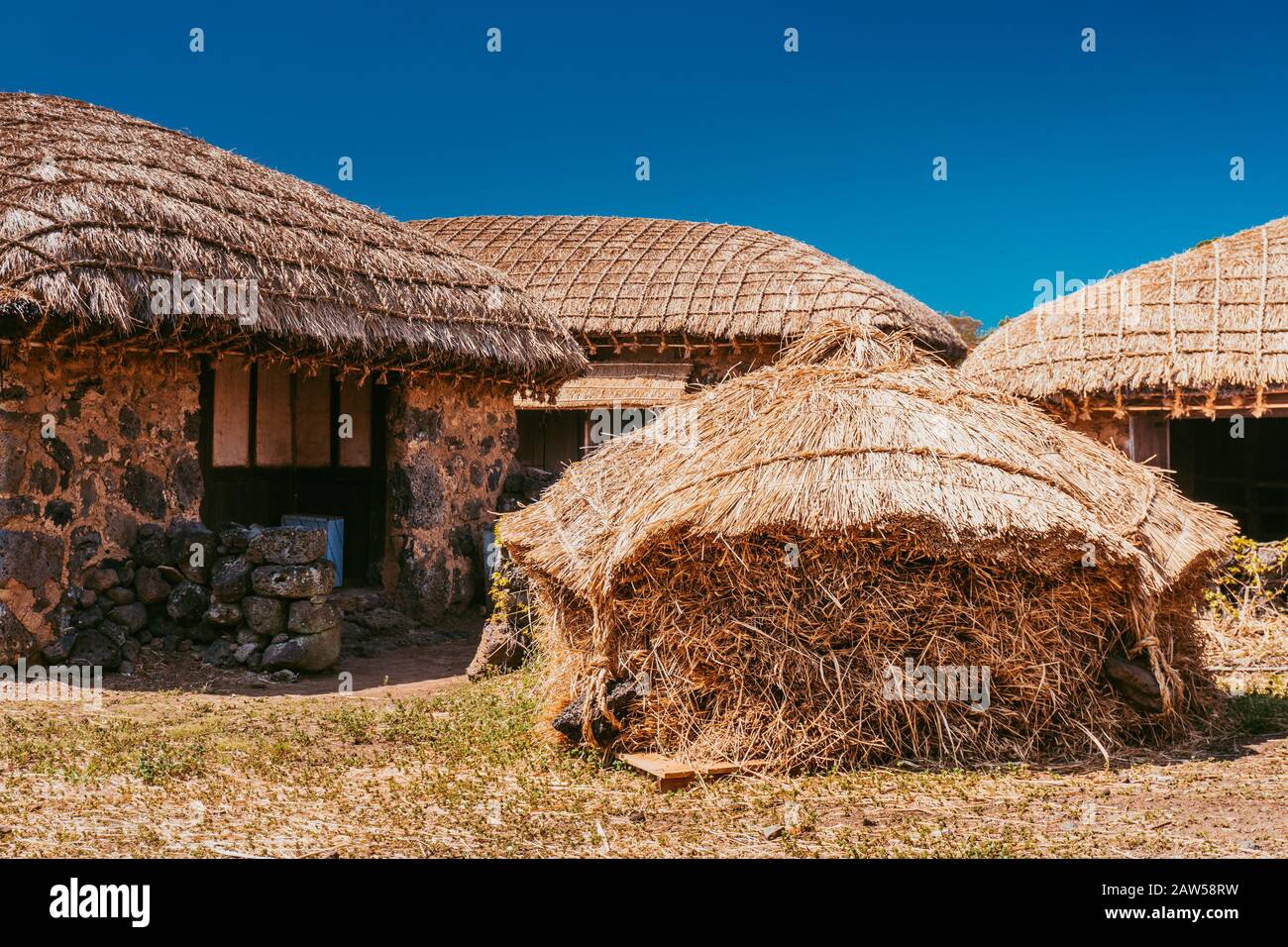 Traditional folk village. Thatched houses and blue sky. Straw hut roofs and clay walls with stones are still in a good condition. Stock Photo