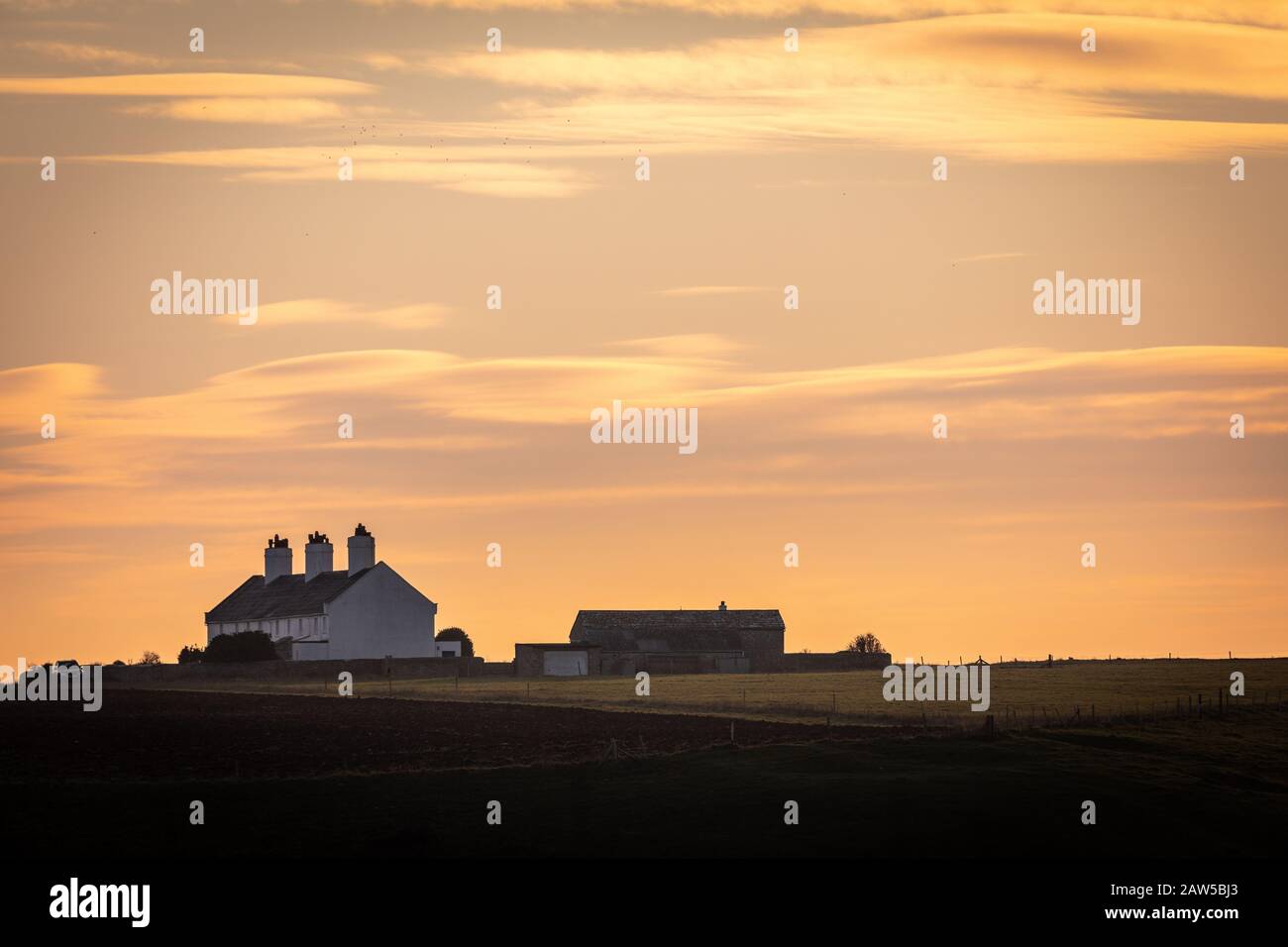 Secluded coast guard cottages with fields and on coastline with beautiful sunset as backdrop Stock Photo