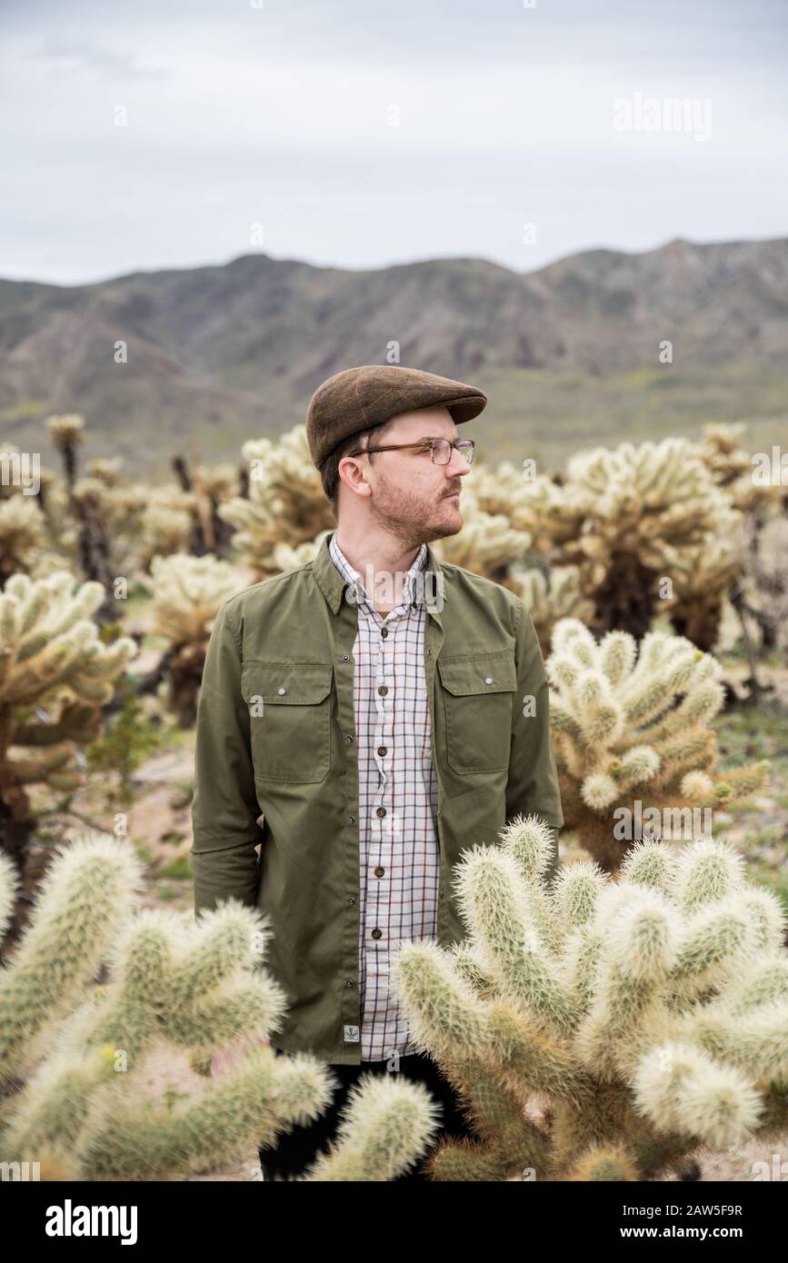 Young man profile in cholla cactus field with hills in the background Stock Photo