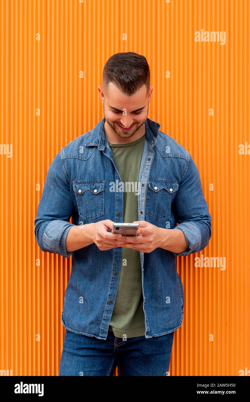 Portrait of a young cool man over orange background. The man is checks his cell phone. Stock Photo