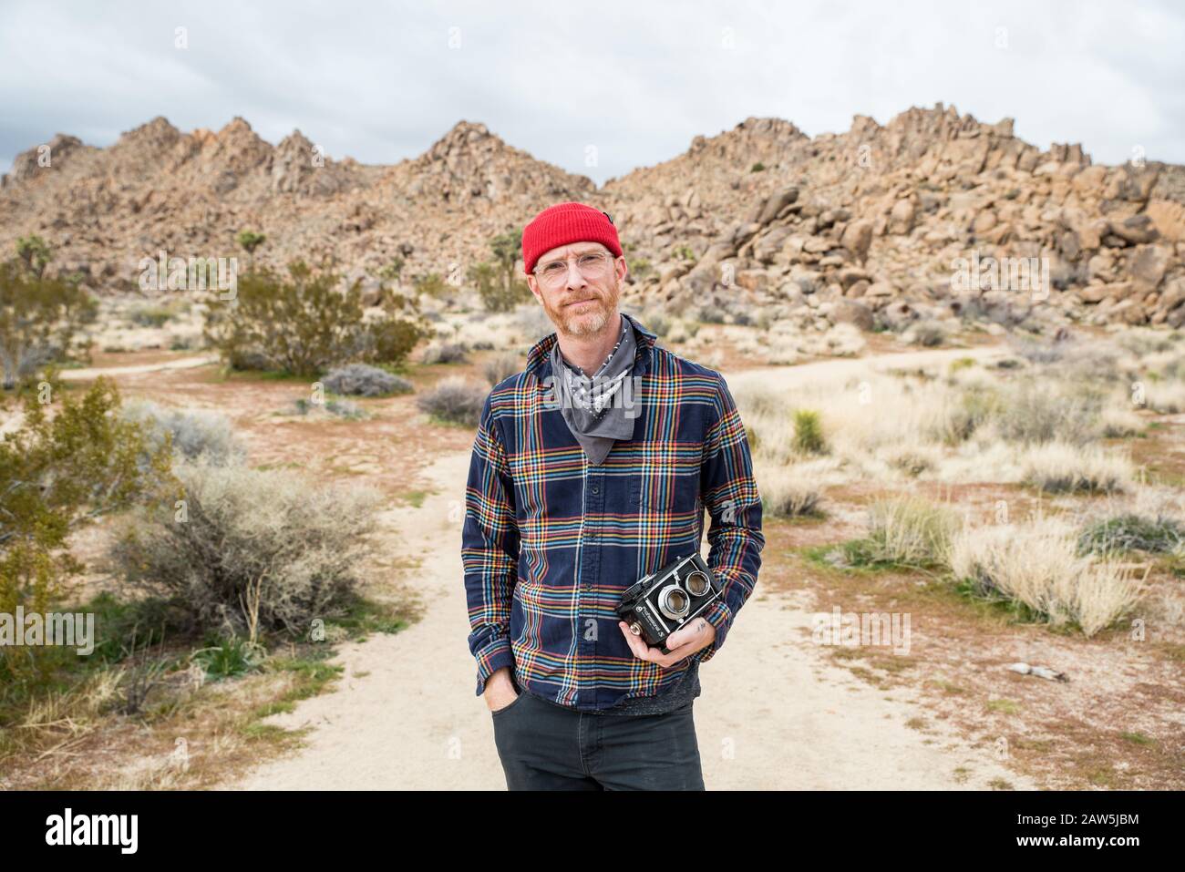 Man in beanie with beard and glasses by far off stone piles in desert Stock Photo