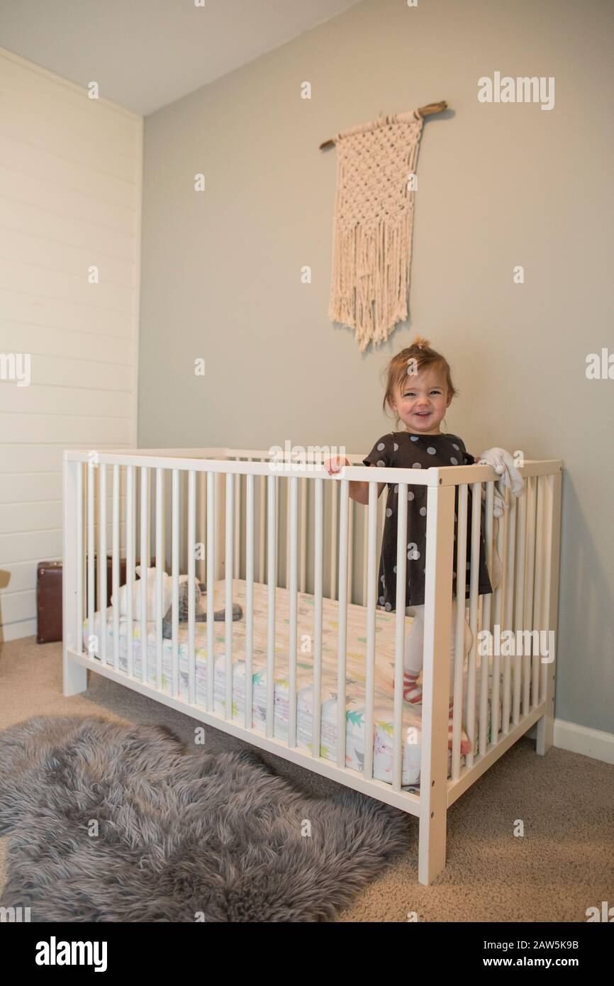 Portrait of cute toddler girl standing inside her crib Stock Photo