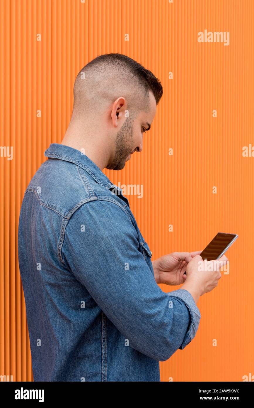 Portrait of a young cool man over orange background. The man is checks his cell phone. Stock Photo