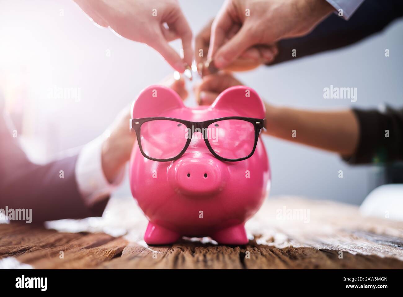 Businesspeople's Hand Inserting Coins Into Pink Piggybank In Office Stock Photo
