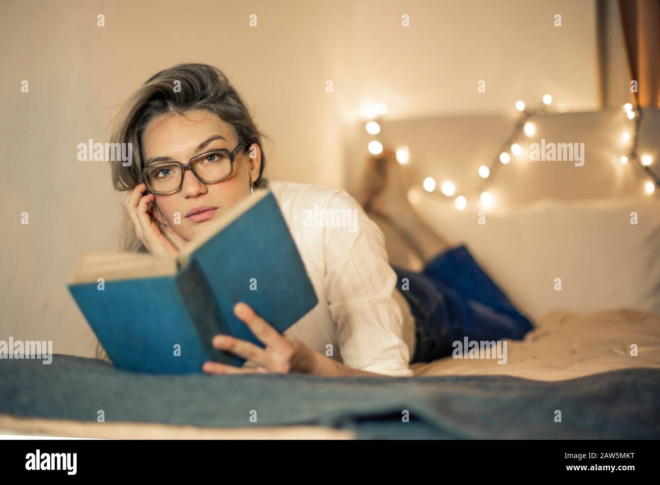 young woman reads a book on a bed Stock Photo
