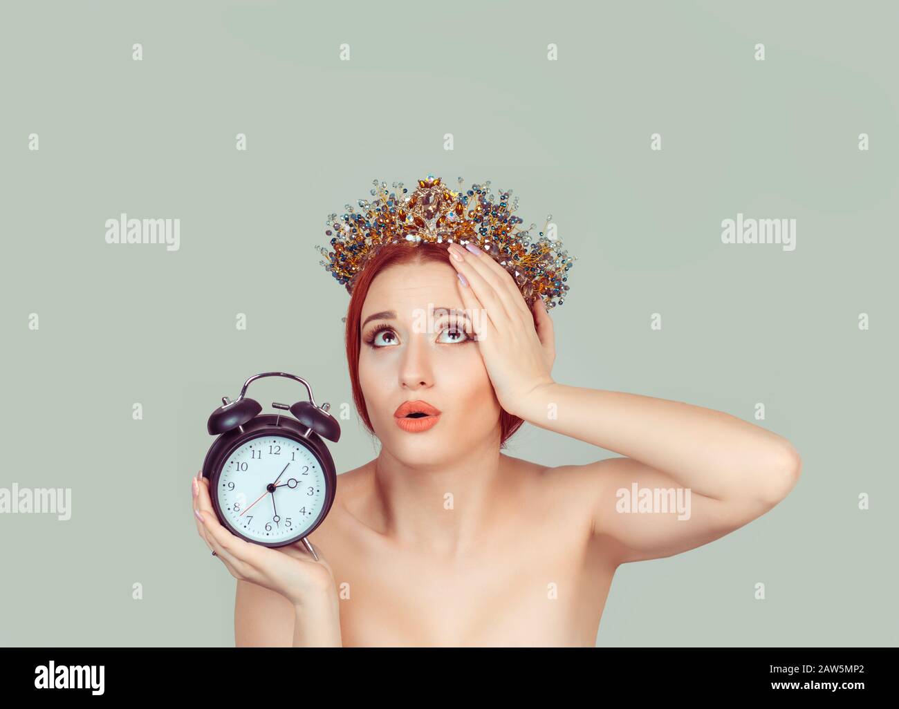 Time ruins my beauty. Anxious young woman looking up holding alarm