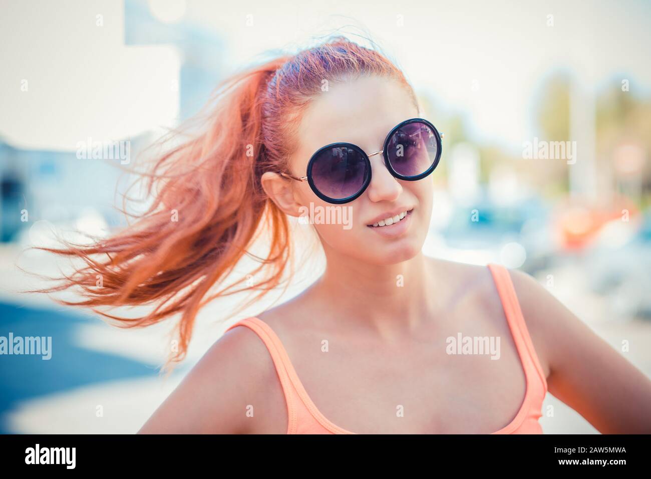 Smiling beautiful young woman in pink shirt and round sunglasses enjoying time outdoors in summer holiday time. beauty outdoor portrait with city stre Stock Photo