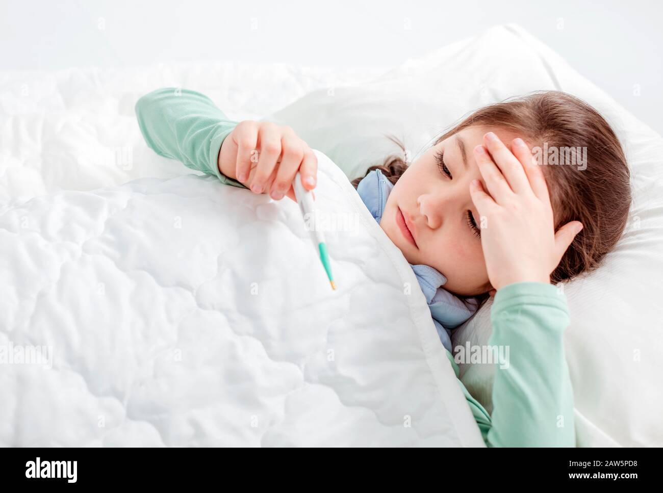 Sick child with flu fever laying in bed and  holding thermometer Stock Photo