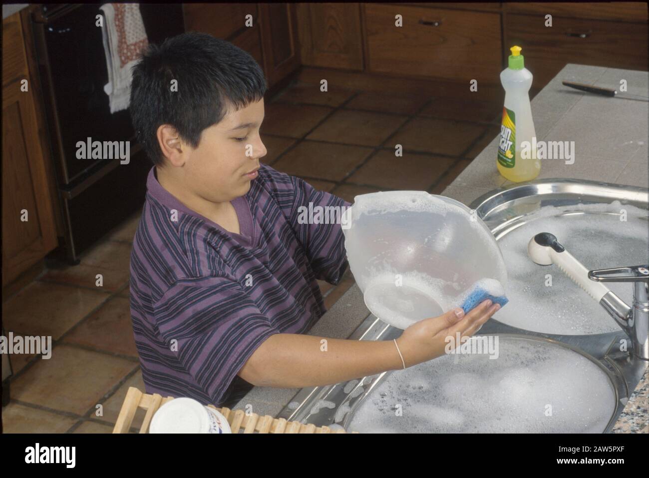 Tenyearold Hispanic boy washing dishes at home in Austin Texas USA