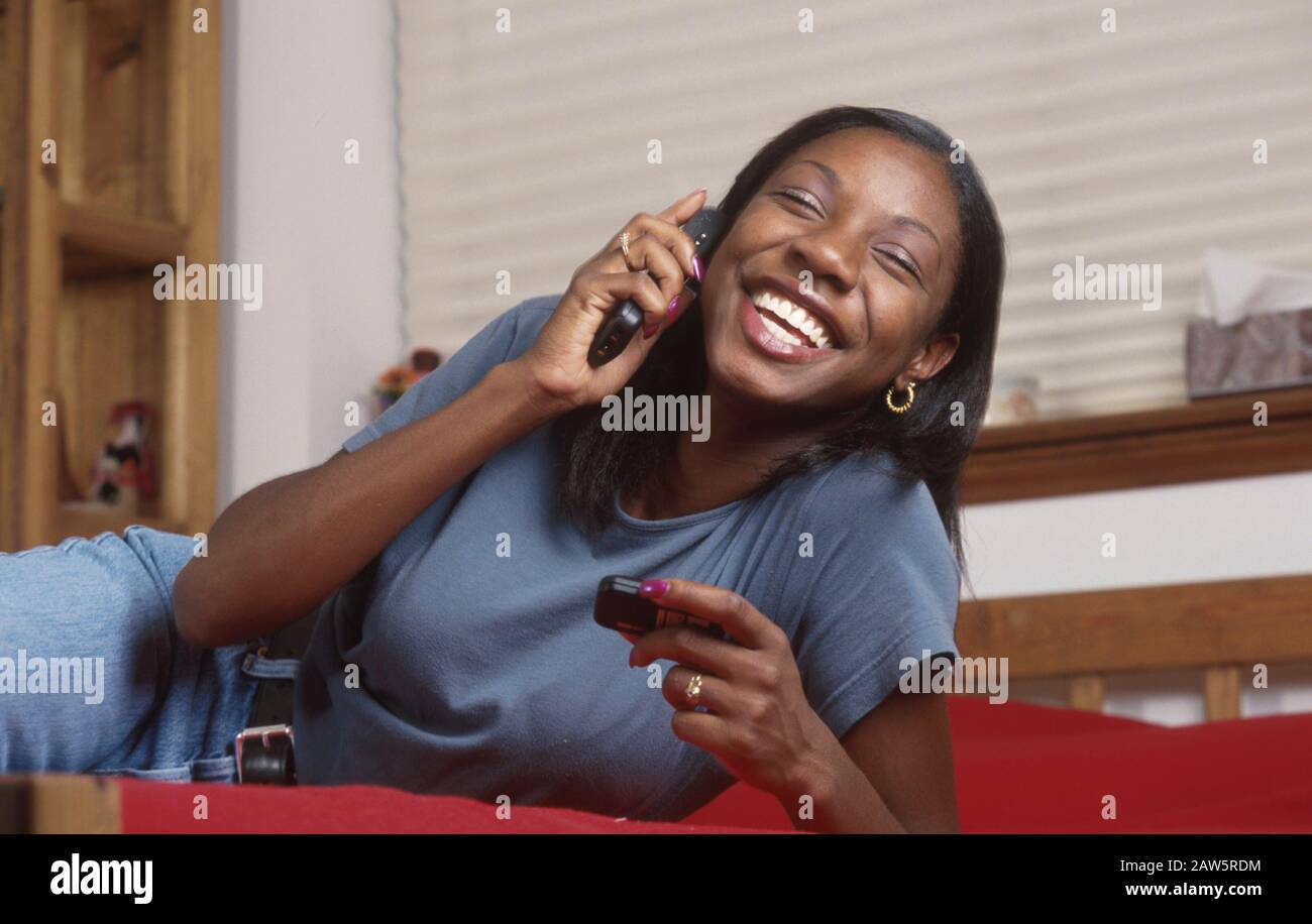 Eighteen-year-old African-American girl talks on cell phone while checking her pager for phone numbers. Stock Photo