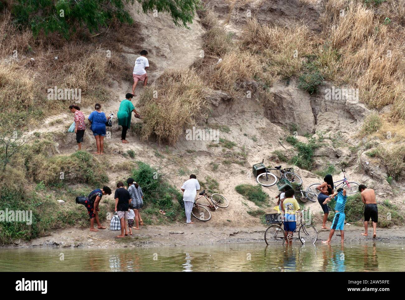 People climbing up a riverside bluff after crossing the Rio Grande from the United States into Mexico, bypassing the official border crossing point from Brownsville, Texas, into Matamoros, Tamaulipas. Stock Photo