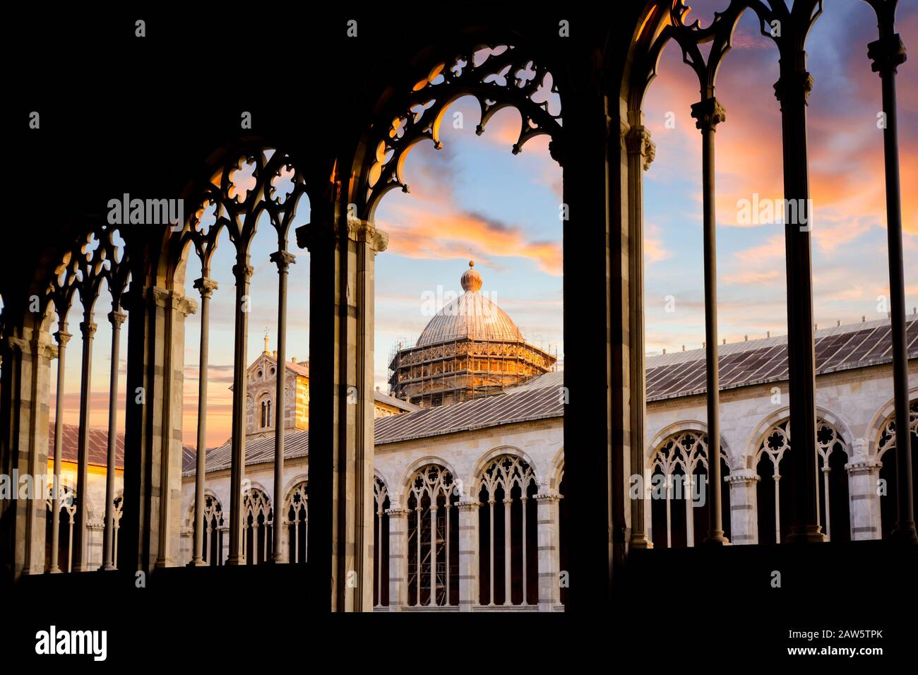 The Duomo Pisa Cathedral dome is visible under a colorful sunset from inside stone arched windows of Camposanto in the Tuscan city of Pisa, Italy. Stock Photo