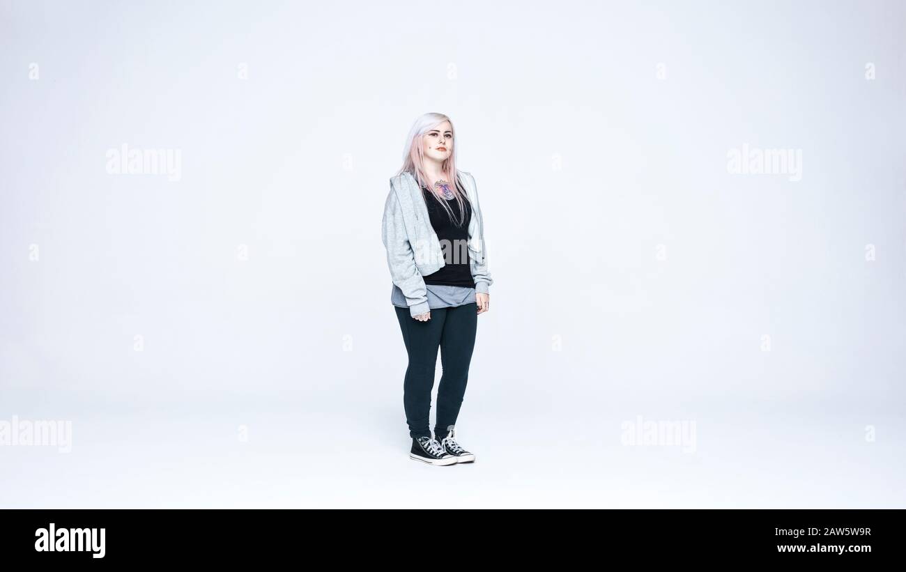 Woman in white hair and tattoo on chest looking at camera. Woman with fashion piercing on cheeks isolated on white background. Stock Photo