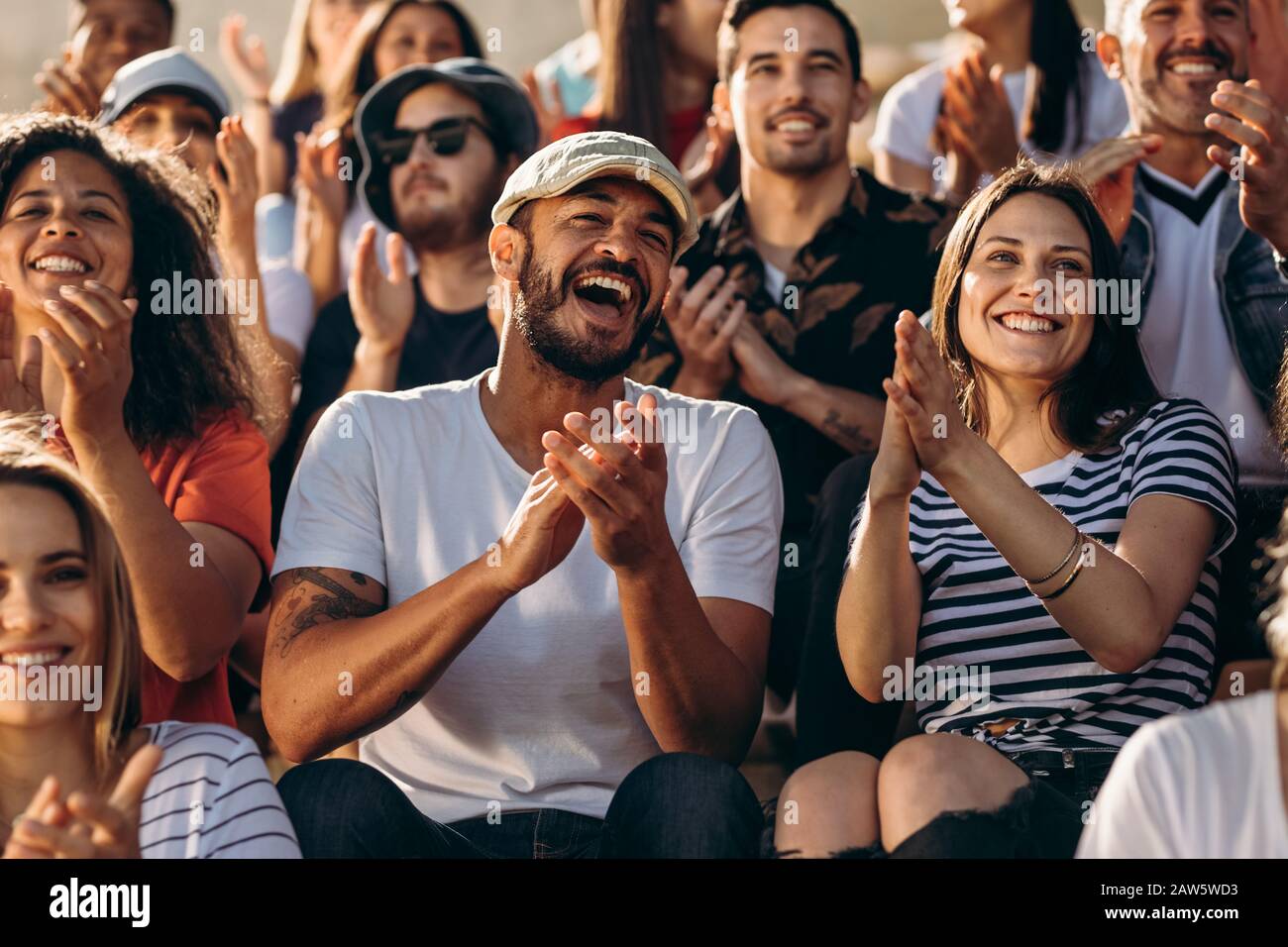 Group of people watching a sport event and cheering. Excited crowd of sports fans applauding sitting in stadium. Stock Photo