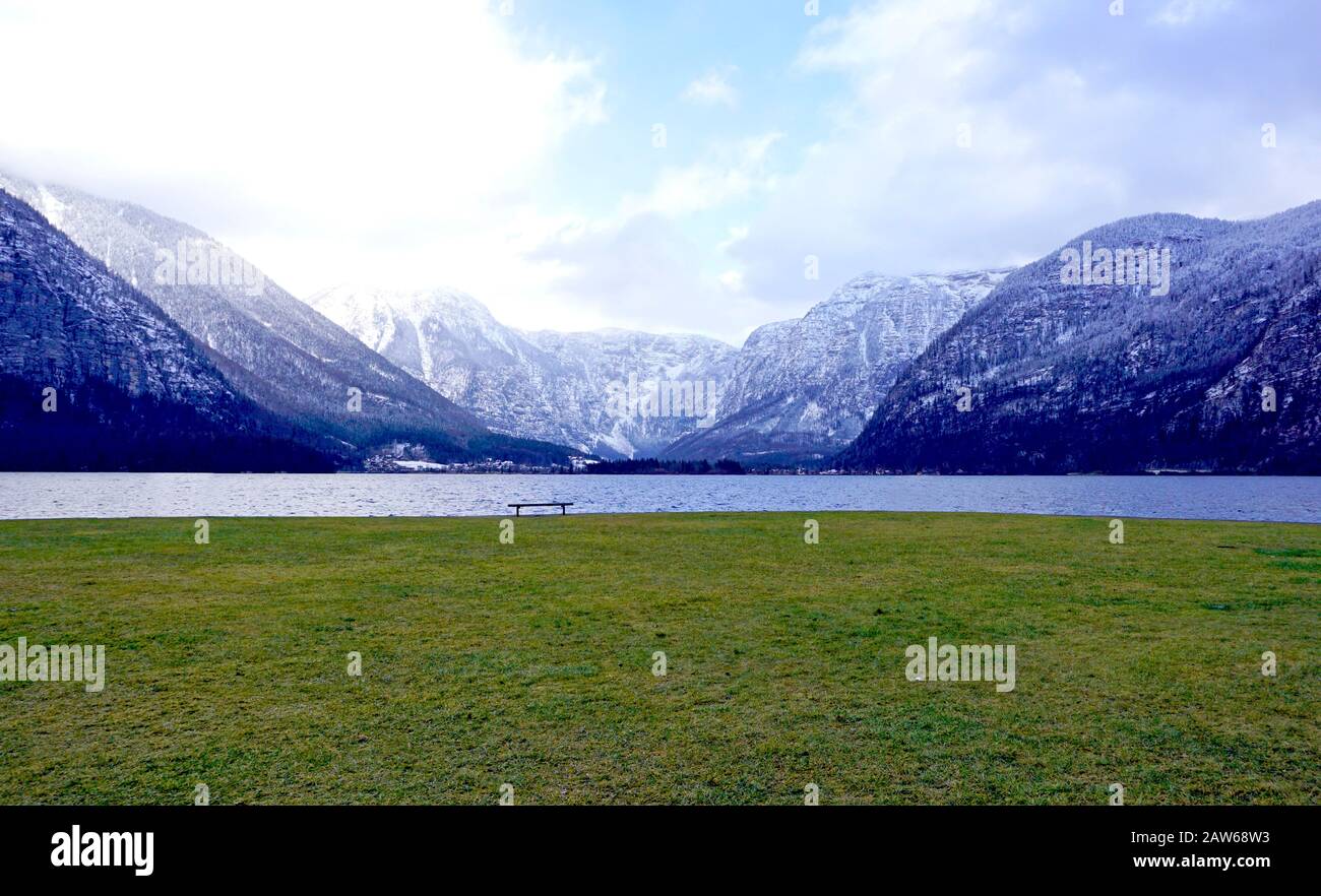 panorama of Hallstatt lake and green grass field outdoor and lonely bench with snow mountain background in Austria in Austrian alps Stock Photo