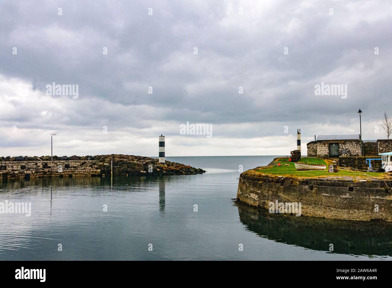 Small harbor in fishing village of Carnlough of Northern Ireland under cloudy skies with a view of sea beyond. Stock Photo