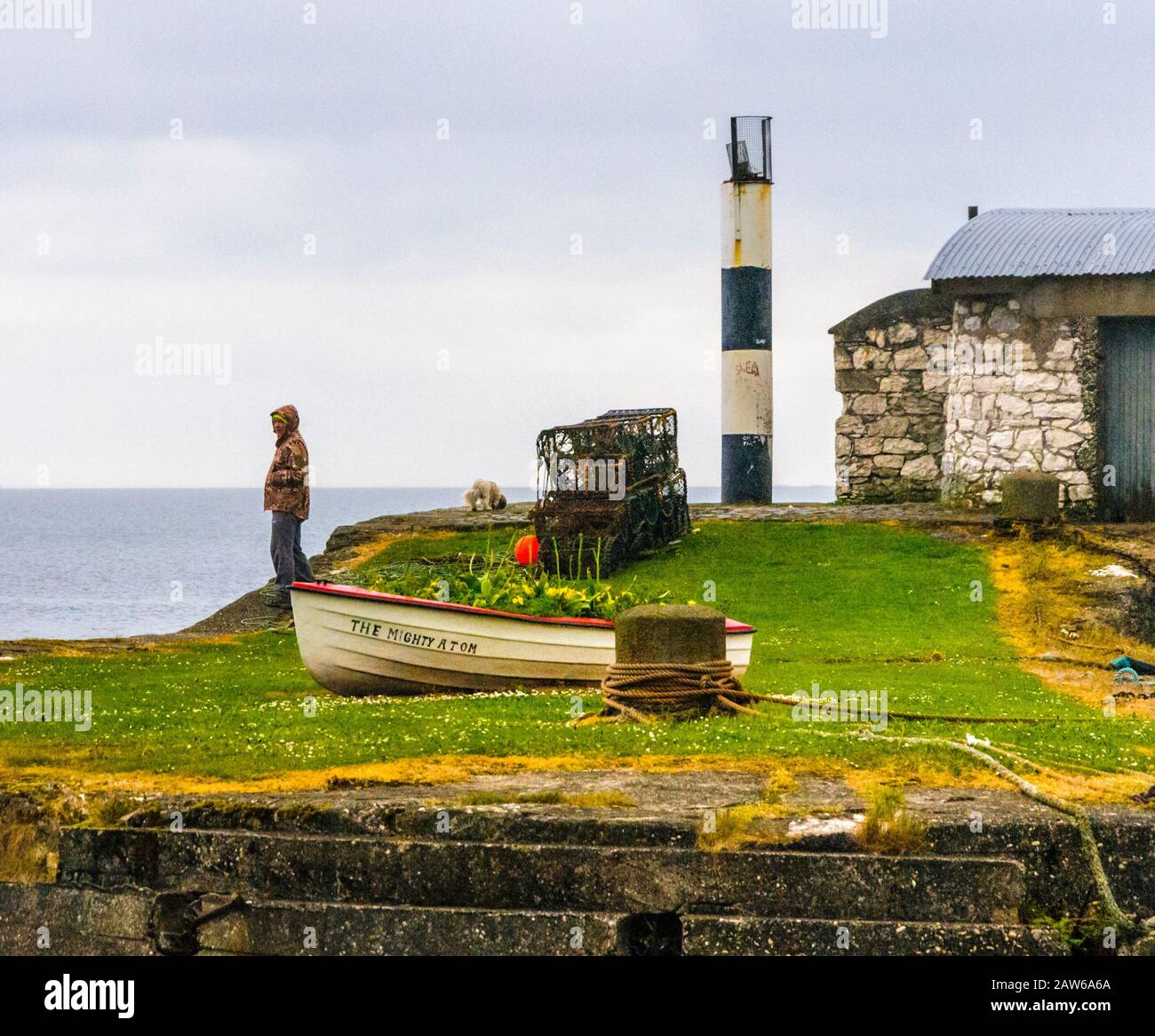 Carnlough-Northern Ireland, UK/May 19-2020:  Small harbor and lighthouse in fishing village under cloudy skies with a view of sea beyond. Stock Photo