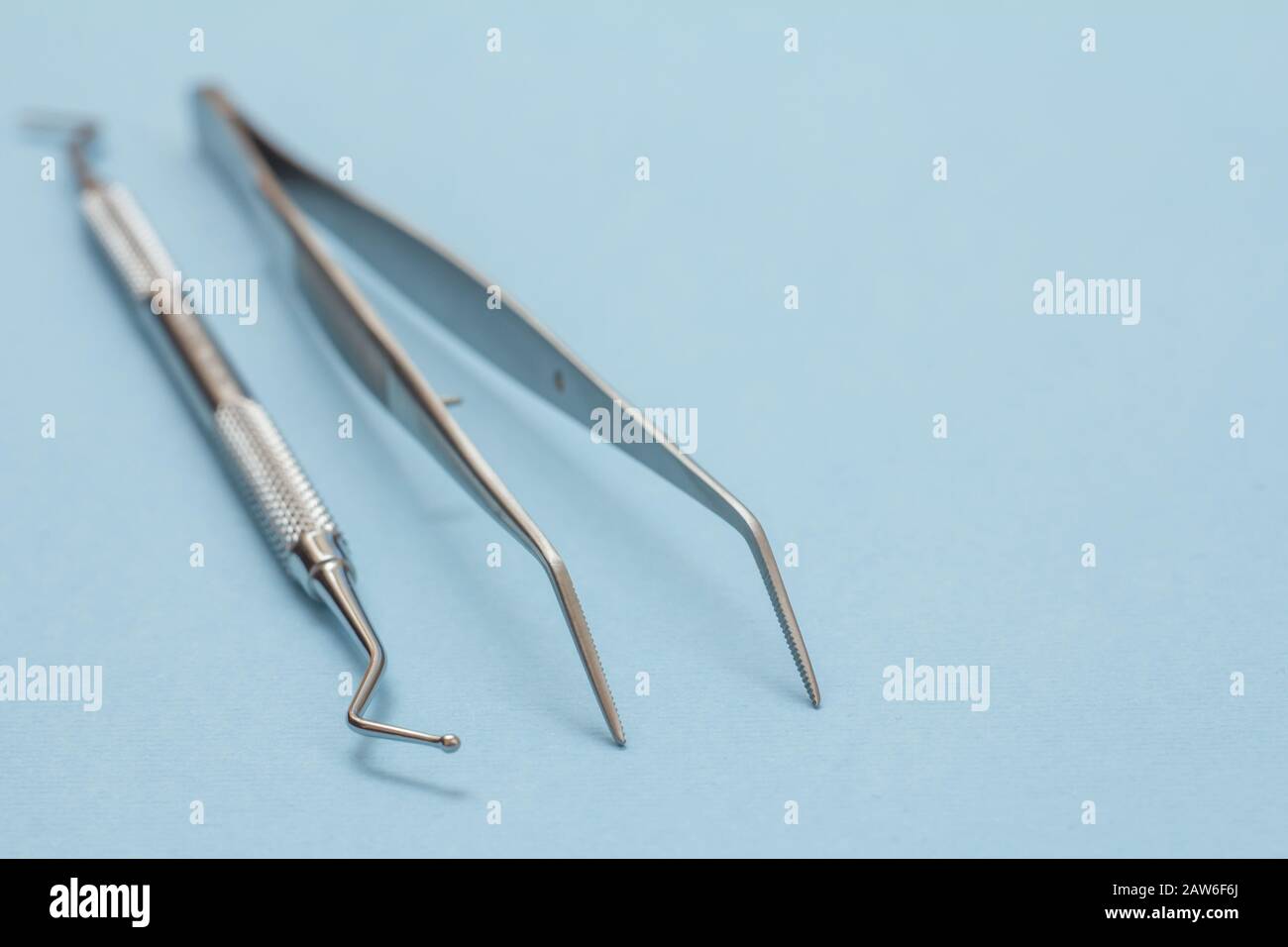 Set of metal dental instruments for dental treatment. Dental plugger and tweezers on blue background. Medical tools. Shallow depth of field. Stock Photo