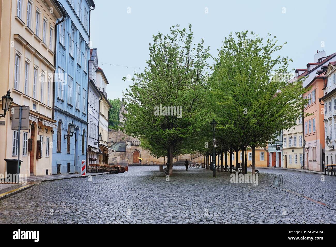 An avenue of trees in a square with a cobbled street framed by apartment buildings. Early spring morning on Na Kampě, Malá Strana, Czechia Prague. Stock Photo