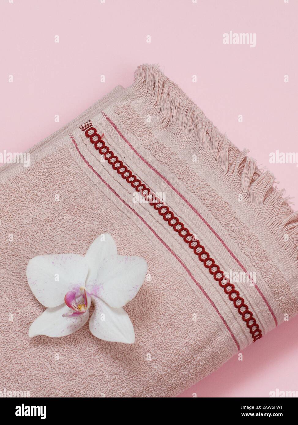 Brown soft terry towel with white orchid bud on pink background. Top view. Stock Photo