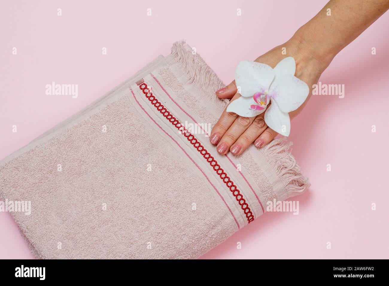 Soft terry towel, woman's hand with white orchid flower on pink background. Top view. Stock Photo