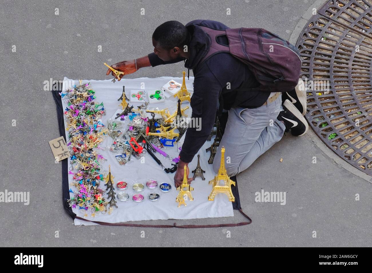 An illegal street vendor selling multi coloured Eiffel Tower souvenirs in Paris kneeling by on an open cloth that converts to a carry bag Stock Photo