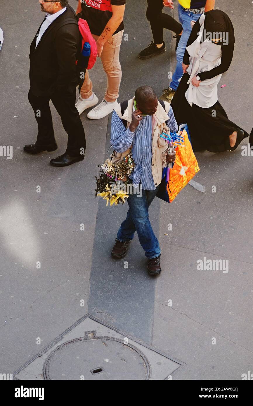 A street vendor souvenir seller at Bir-Hakeim metro stands with arms full of miniature Eiffel Tower souvenirs as people pass behind, viewed from above Stock Photo