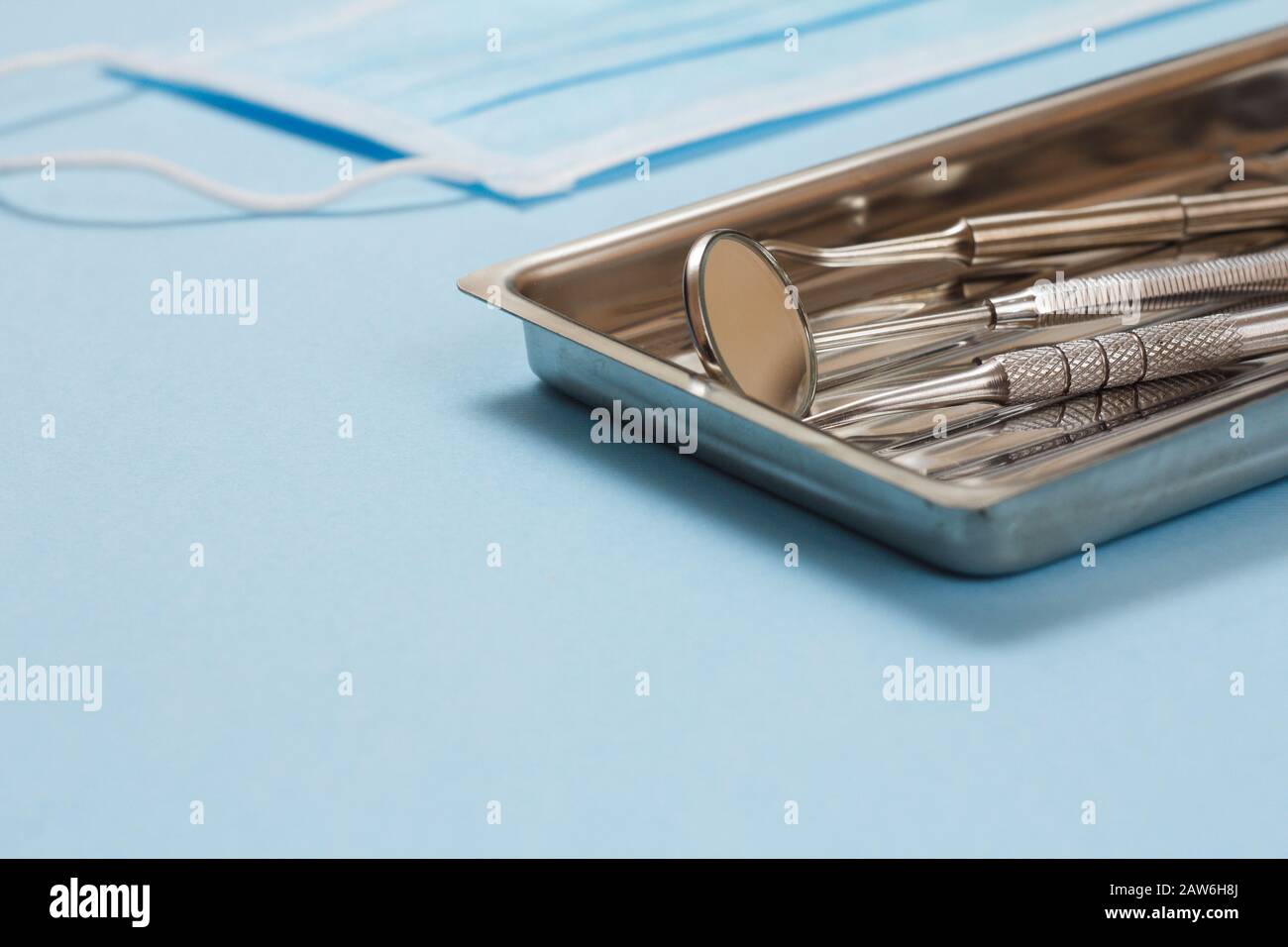 Set of composite filling instruments for dental treatment. Medical tools in stainless steel tray and a mask on blue background. Shallow depth of field Stock Photo