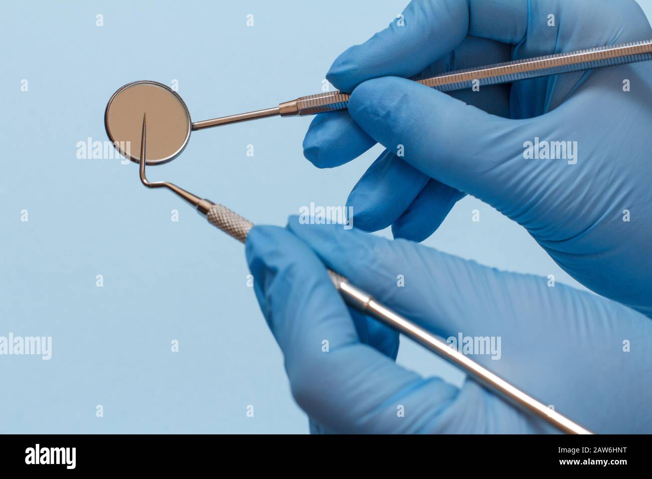 Dentist's hands in rubber gloves with probe and mouth mirror on blue ...