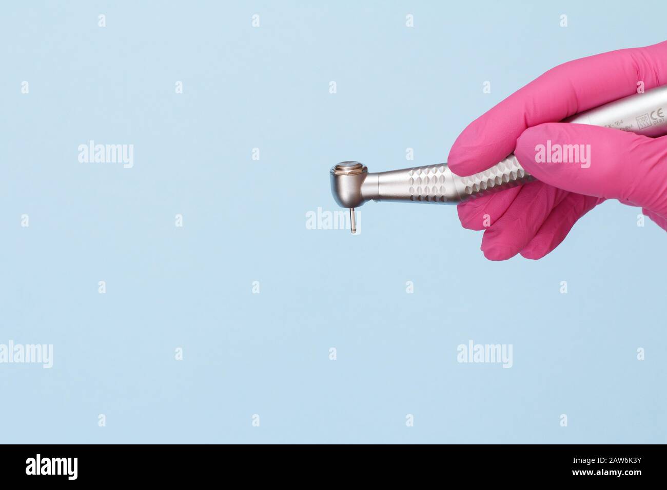 Dentist's hand in a pink rubber glove with high-speed dental handpiece on blue background. Medical tools concept. Stock Photo