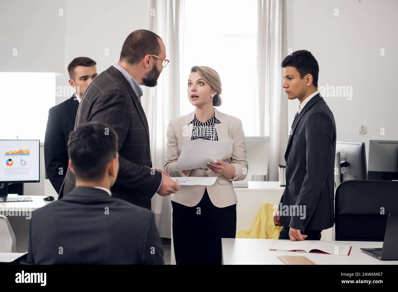 Young woman in suit with documents in her hands talk agressively with her chief, coworkers stand around them in the office Stock Photo