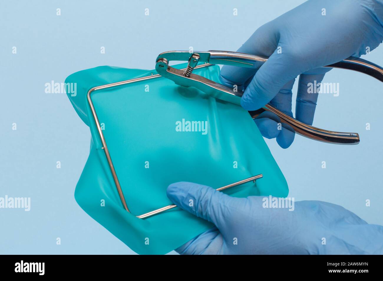 Dentist's hands in a latex gloves with dental punch, cofferdam scarf and frame on blue background. Medical tools concept. Stock Photo