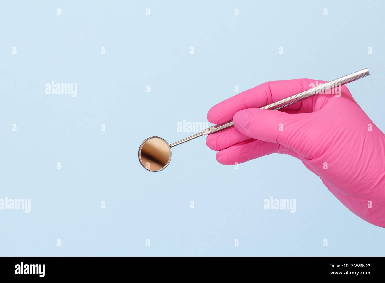 Dentist's hand in a pink latex glove with mouth mirror on blue background. Medical tools concept. Stock Photo