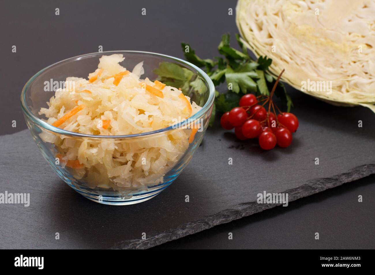 Homemade fermented cabbage with carrot in glass bowl. Fresh head of cabbage and cluster of viburnum on the background. Vegan salad. Dish is rich in vi Stock Photo
