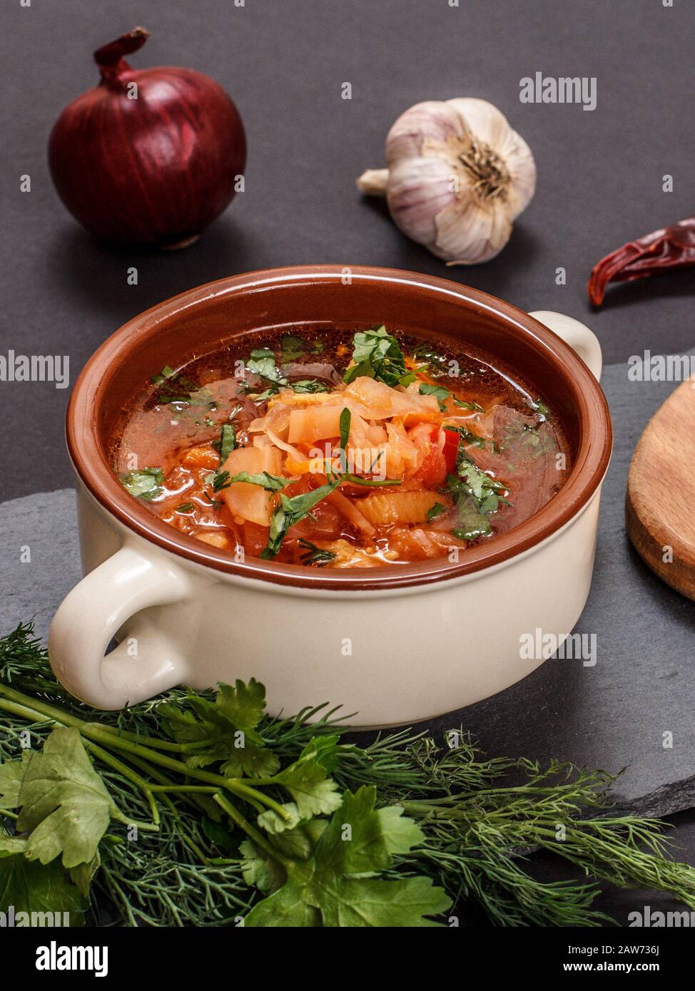Ukrainian traditional borsch in porcelain bowl with parsley, onion, garlic and capsicum on stone board. Top view. Stock Photo