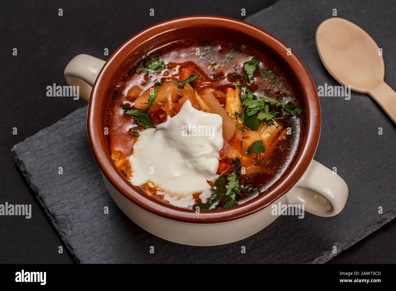 Ukrainian traditional borsch with sour cream in porcelain bowl with wooden spoon on stone board. Top view. Stock Photo