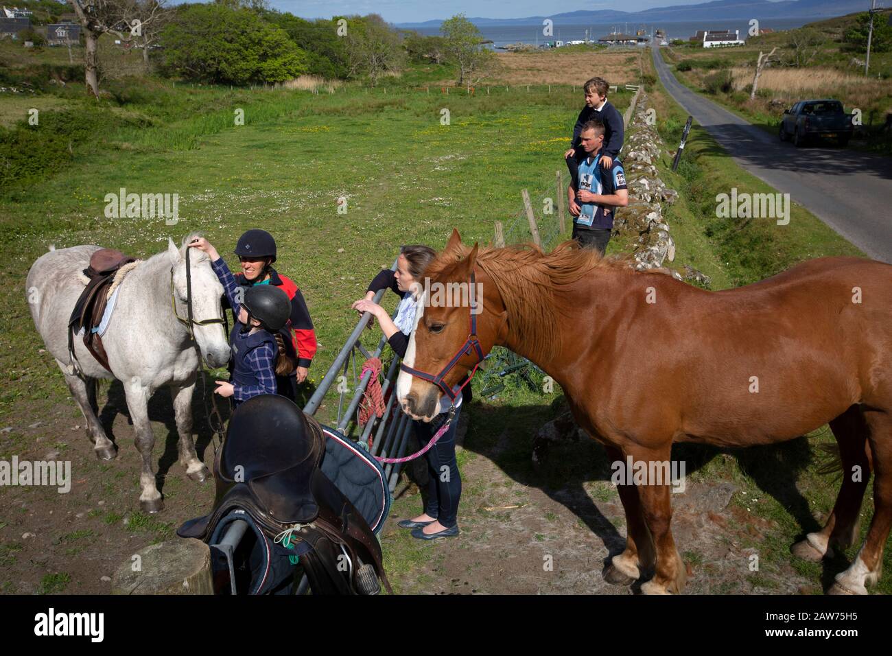 Local GP Jan Brooks (second left) giving a riding lesson to an islander on the the Inner Hebridean island of Colonsay on Scotland's west coast.  The island is in the council area of Argyll and Bute and has an area of 4,074 hectares (15.7 sq mi). Aligned on a south-west to north-east axis, it measures 8 miles (13 km) in length and reaches 3 miles (4.8 km) at its widest point, in 2019 it had a permanent population of 136 adults and children. Stock Photo
