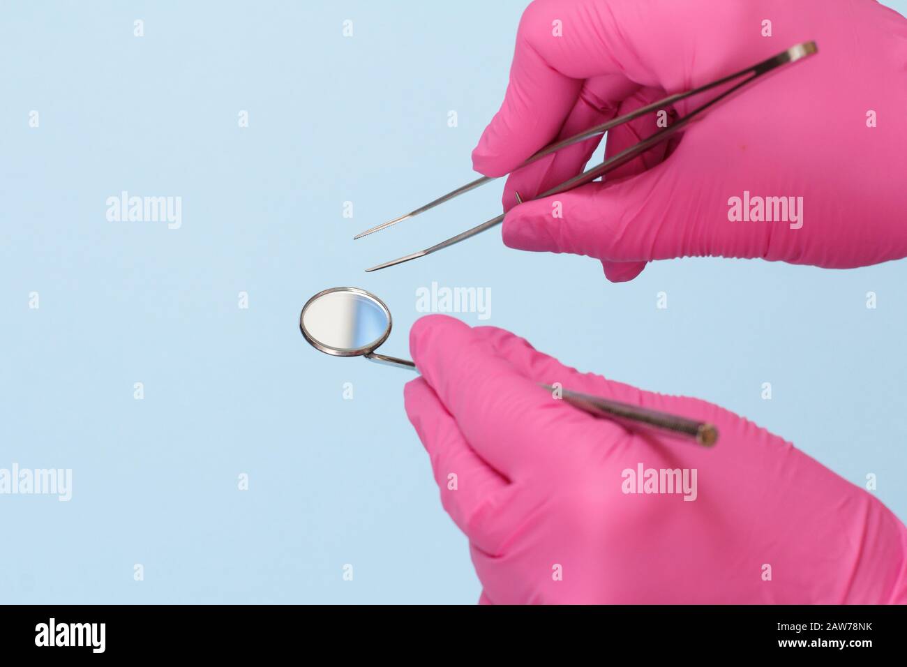 Dentist's hands in pink latex gloves with tweezers and mouth mirror on blue background. Medical tools concept. Stock Photo