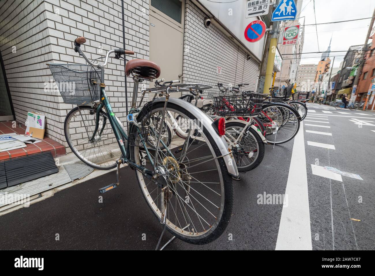 Tokyo, Japan - August 29, 2016: Bicycles parked at roadside in a row with Japanese street signs on the background Stock Photo