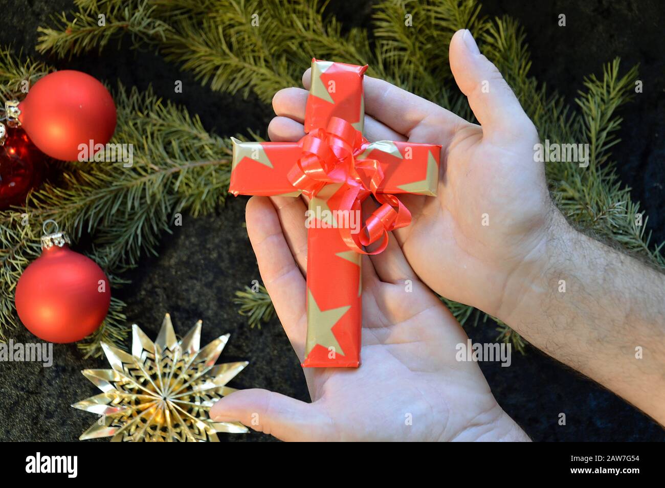 hands offering a cross wrapped in paper as a present at Christmas day Stock Photo