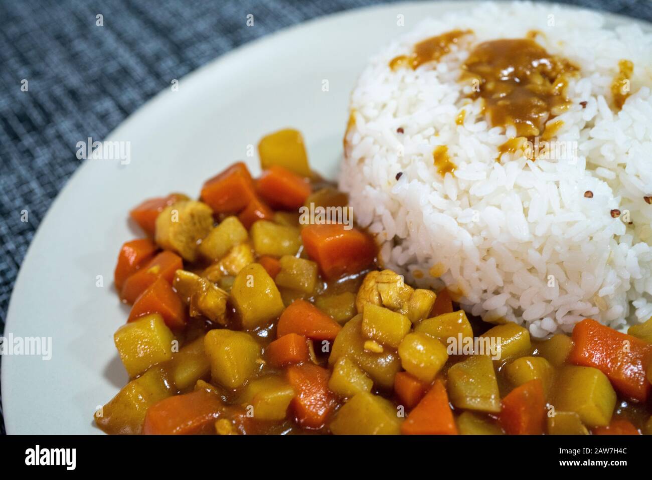 Cooked rice, curry with chicken, carrot and potato close-up on a plate on a table. Stock Photo