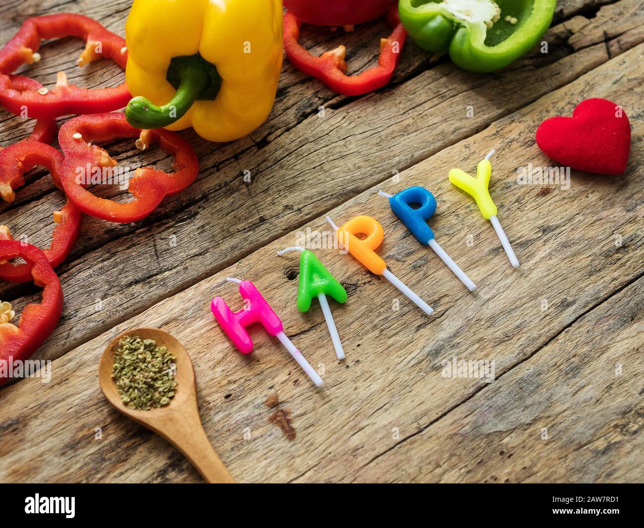 flat lay of cooking utensils with herbs , colorful bell pepper and word happy from candles over wooden background. top view with copy space. enjoy eat Stock Photo