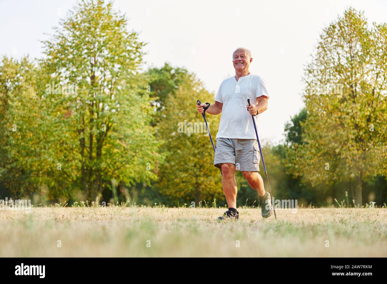 Senior smiling while hiking in summer with walking sticks Stock Photo