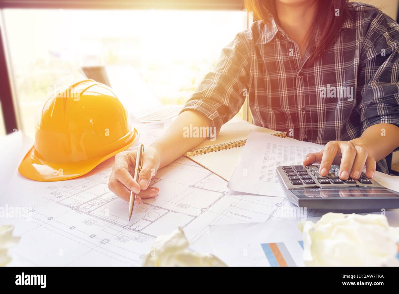 Asian engineer , architect woman using calculator for accounting and analyzing building structure from blueprint and paper chart in front of computer Stock Photo