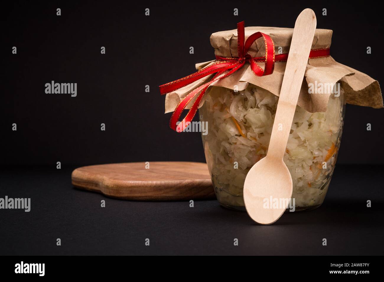 Homemade fermented cabbage with carrot in glass jar on wooden cutting board in black background. Vegan salad. Dish is rich in vitamin U. Food great fo Stock Photo