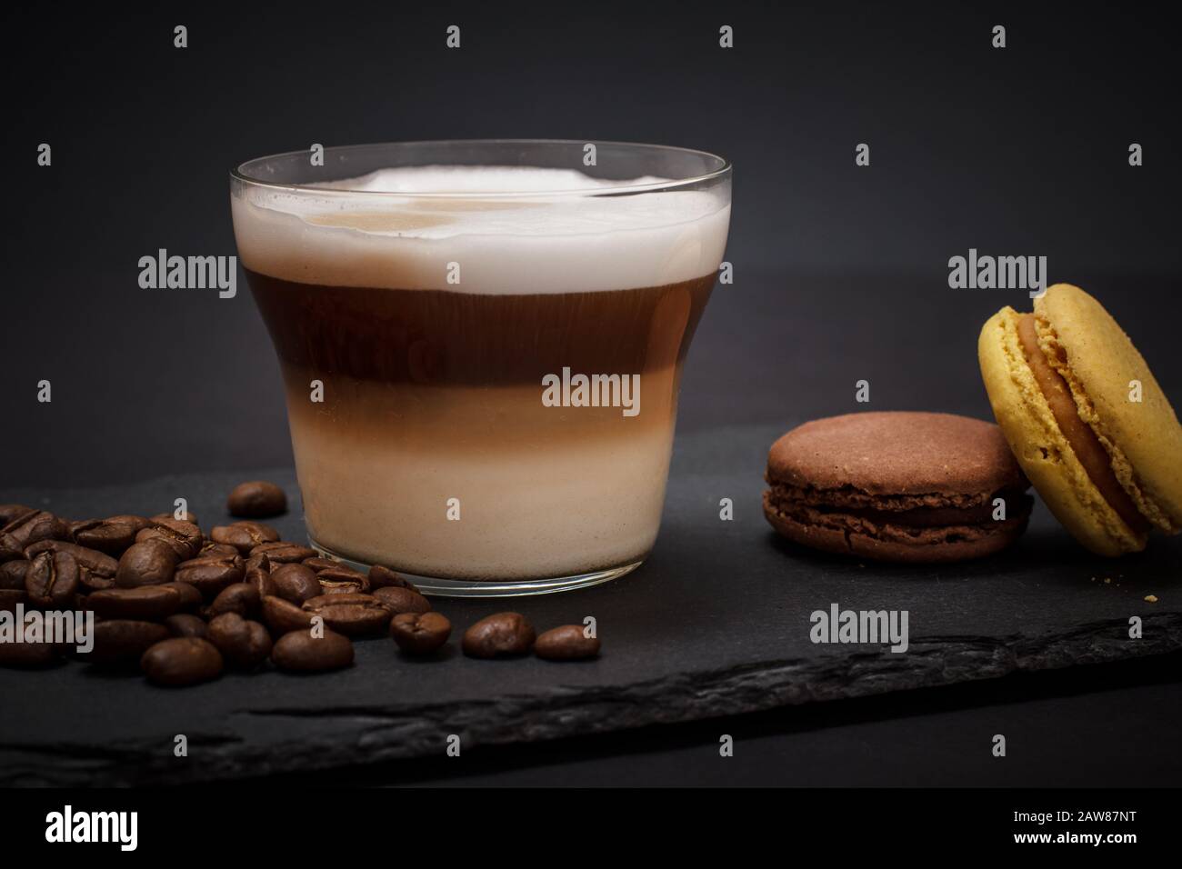 Cup of cappuccino, coffee beans and macaroons on black background. Stock Photo