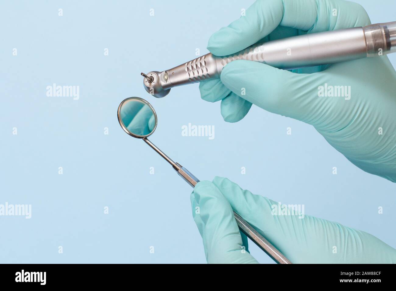 Dentist's hands in pink latex gloves with high-speed dental handpiece and mouth mirror on blue background. Medical tools concept. Stock Photo